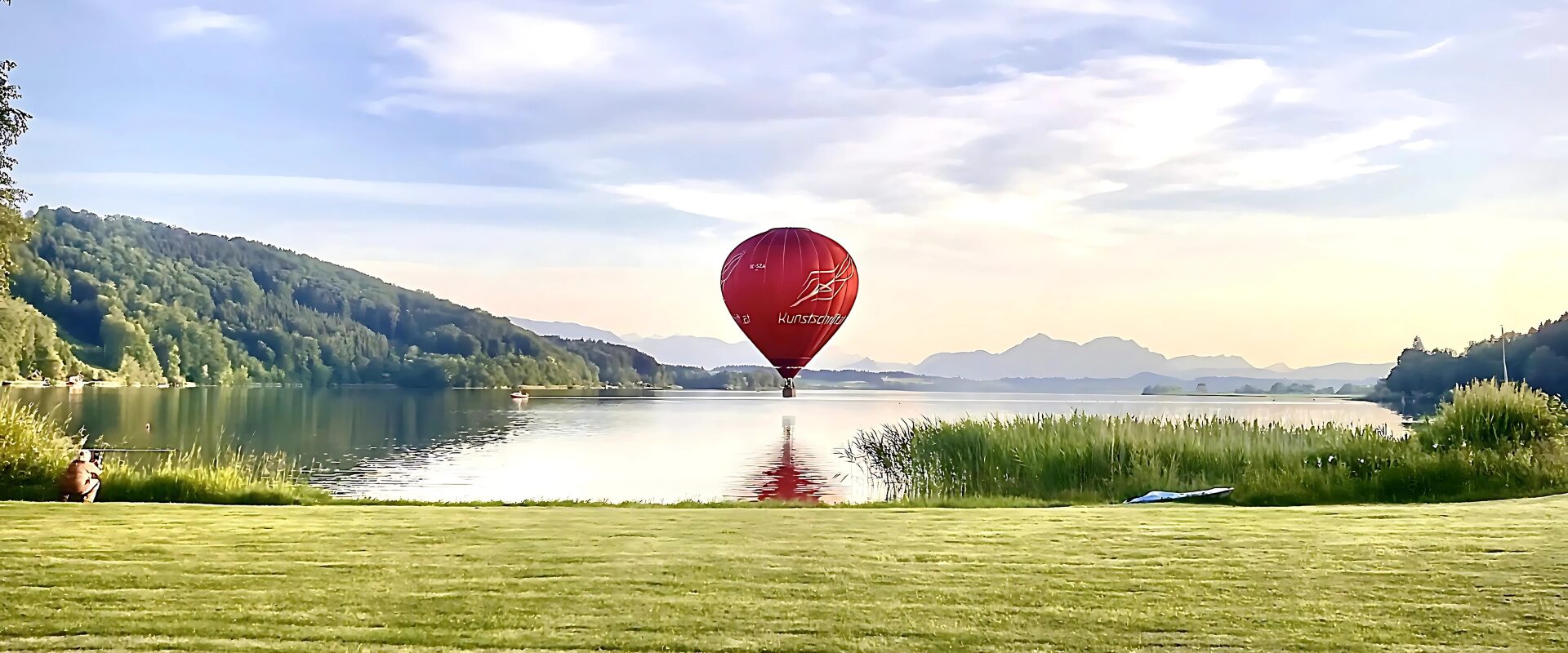 Landschaftsaufnahme mit Heißluftballon Ein Heißluftballon schwebt über einen ruhigen See, umgeben von wunderschöner Natur
